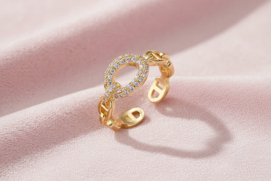 Gold-plated brass chain link ring with one oval CZ-pavé segment on cream background, adjustable cuff style.