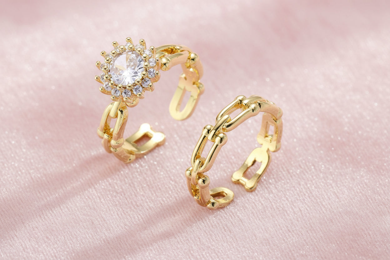 Two adjustable gold rings: chain-link band and halo-style ring with cubic zirconia stones on cream background