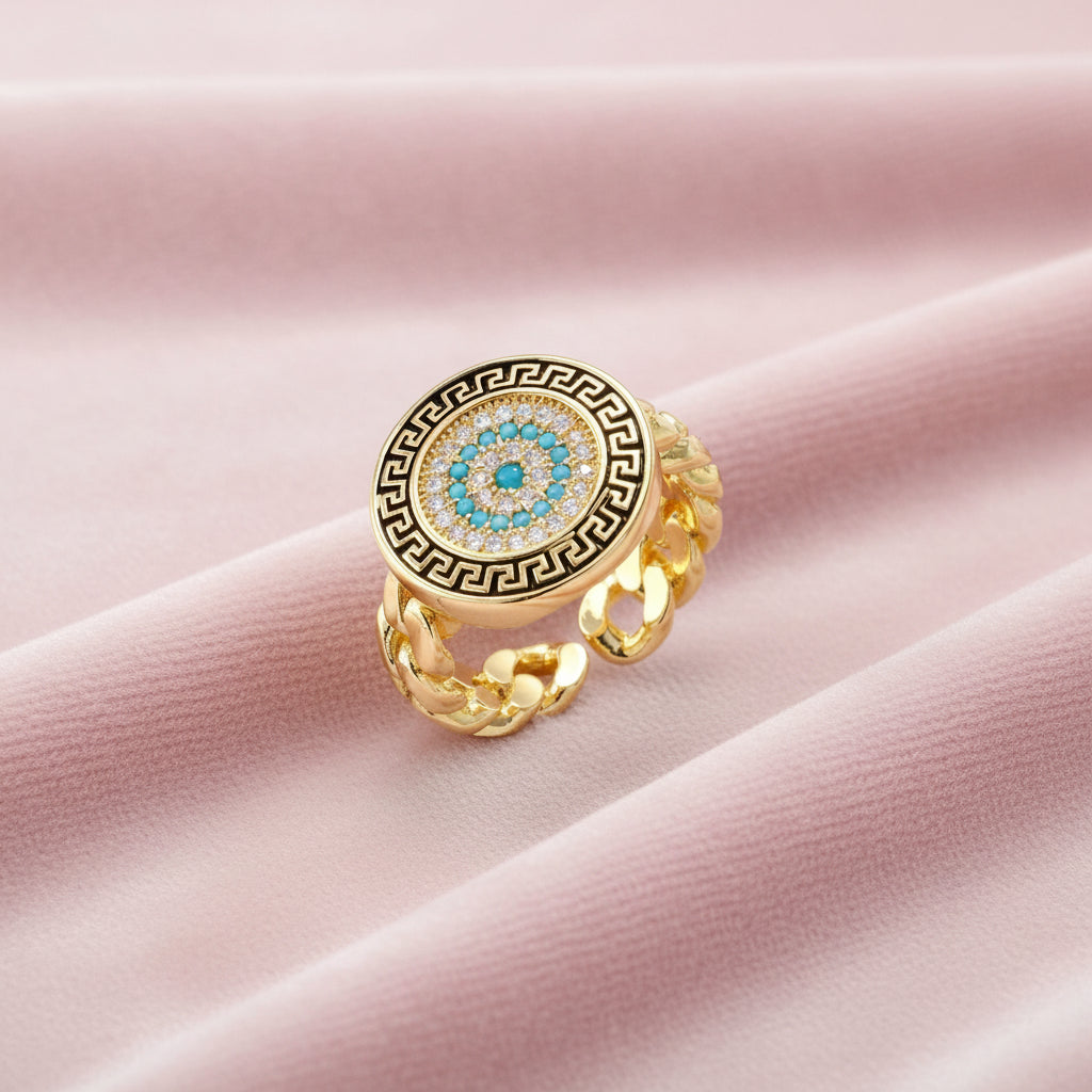 Gold chain ring with Greek key border and turquoise evil eye center on white background