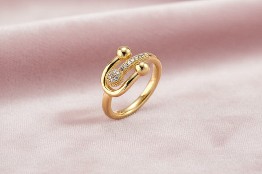 Gold-plated brass ring with safety pin design featuring pavé cubic zirconia stones and dual sphere ends