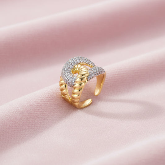 Chunky gold-plated chain-link ring with curved segments and sparkling zirconia crystals on neutral background