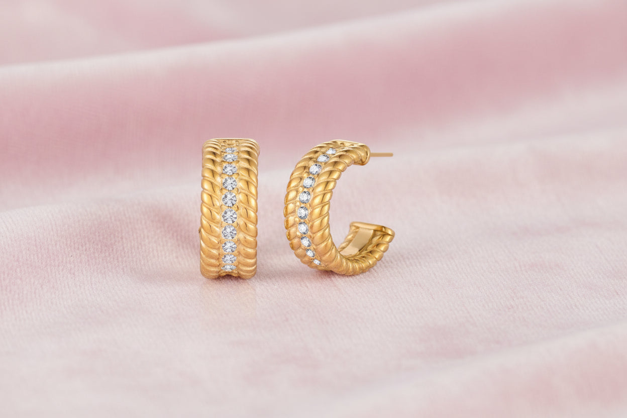 Textured gold huggie hoop earrings with raised ribbed rows creating dimensional sculptural design on cream background